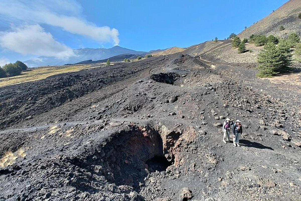 dues persones caminant per un turó de terra amb un forat