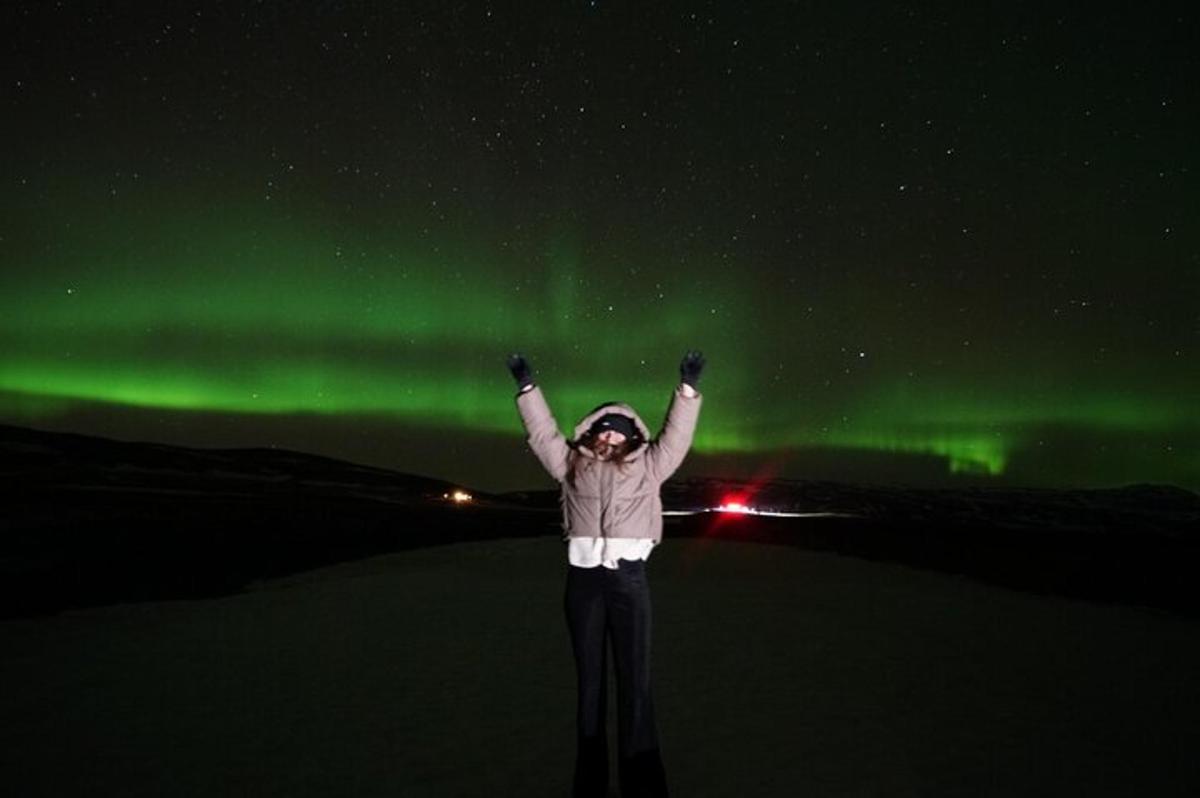Una mujer está de pie bajo la aurora boreal verde.