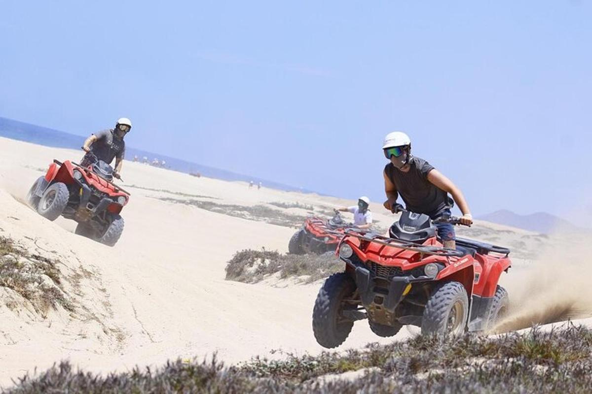 Dos personas conduciendo vehículos todo terreno por la arena del desierto.