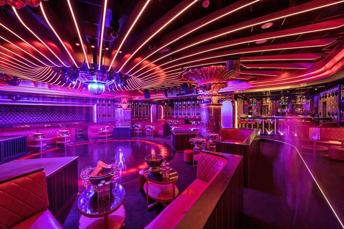 una discoteca con un bar con illuminazione rosa e tavoli