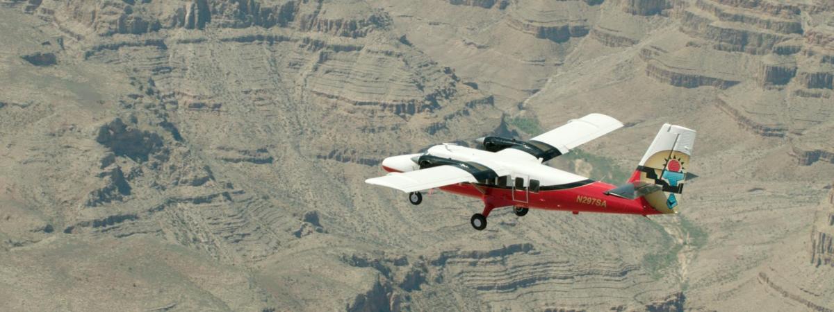 ein kleines rot-weißes Flugzeug, das über einen Canyon fliegt