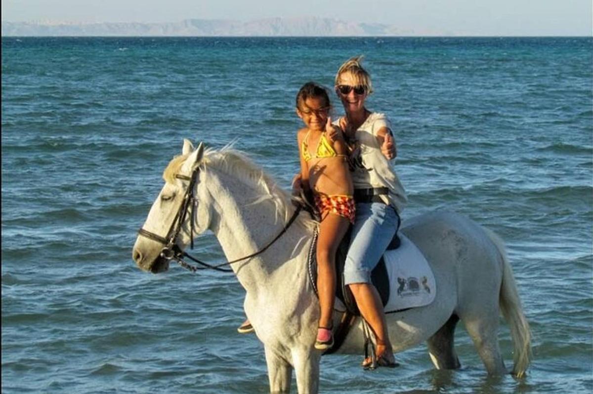 eine Frau und ein Mädchen reiten auf einem Pferd am Strand