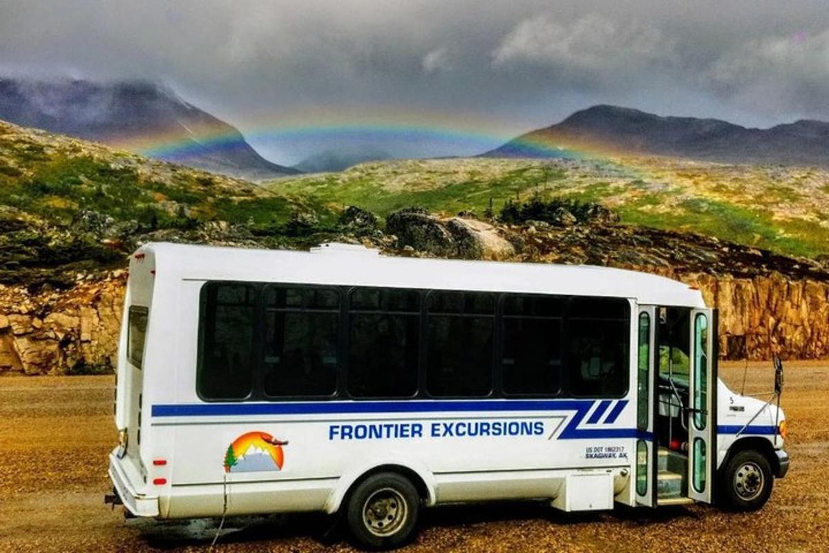 a bus parked in a field with a rainbow in the background