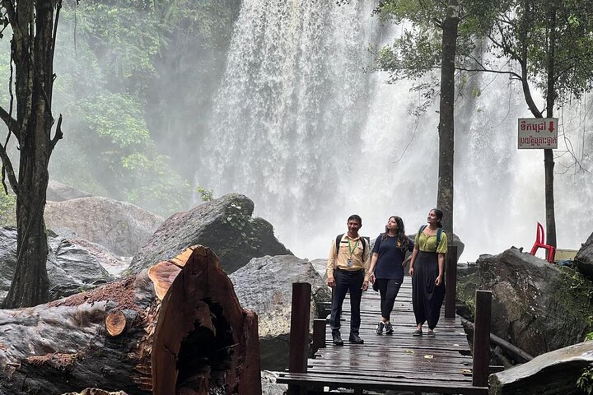 three people standing on a bridge in front of a waterfall