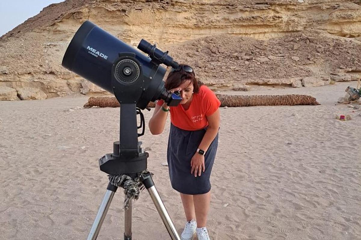 egy nő egy háromlábú távcsövön keresztül néz