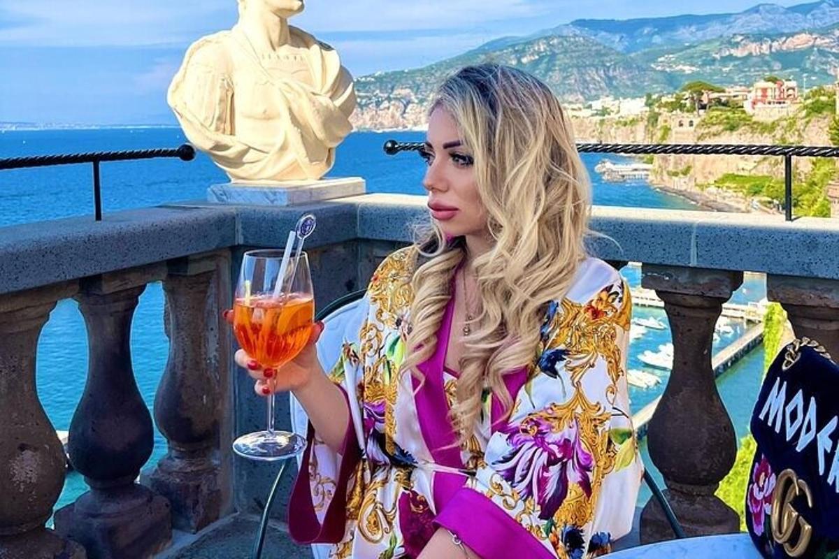 ženska sedi na balkonu in drži kozarec vina v roki