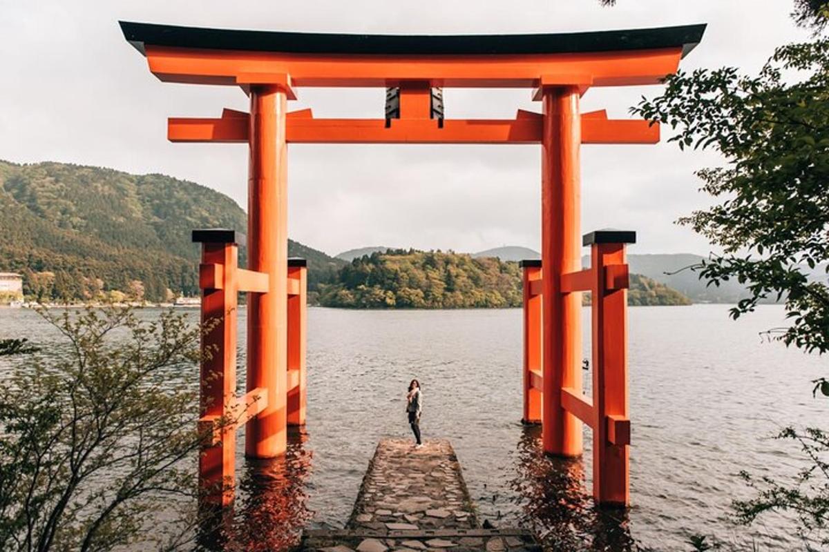Egy személy áll a vízben egy narancssárga torii kapu alatt