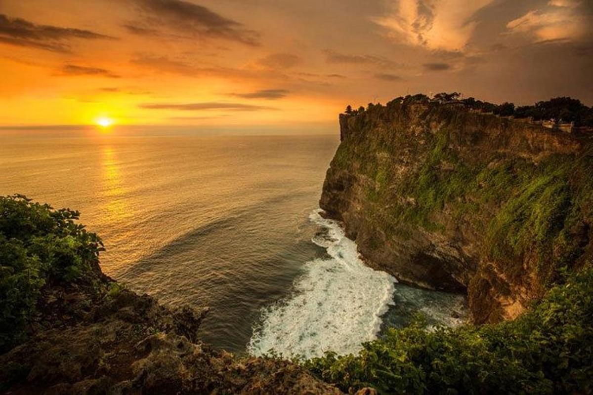 matahari terbenam di atas lautan dengan tebing