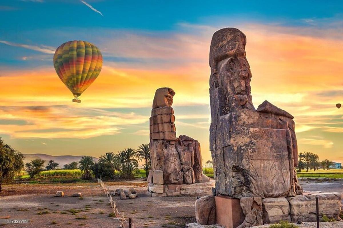 karstā gaisa balons lido pāri divām statujām ar balonu