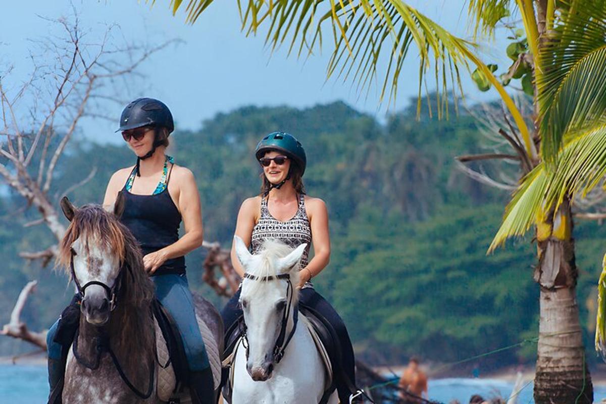 Dos mujeres montando a caballo cerca de una palmera