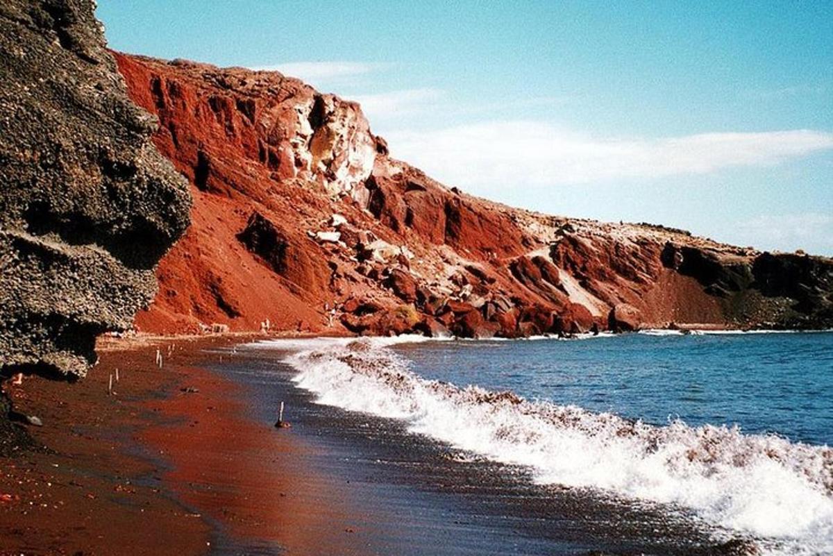 uma praia com um penhasco vermelho e o oceano