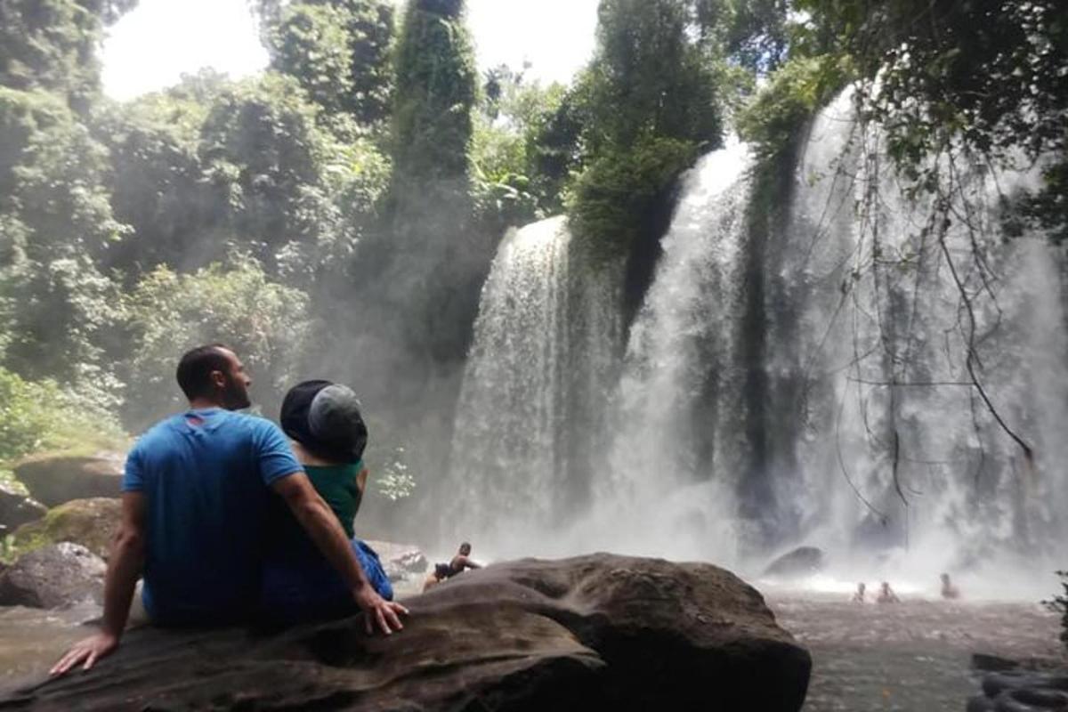 un home i una dona asseguts en una roca davant d'una cascada