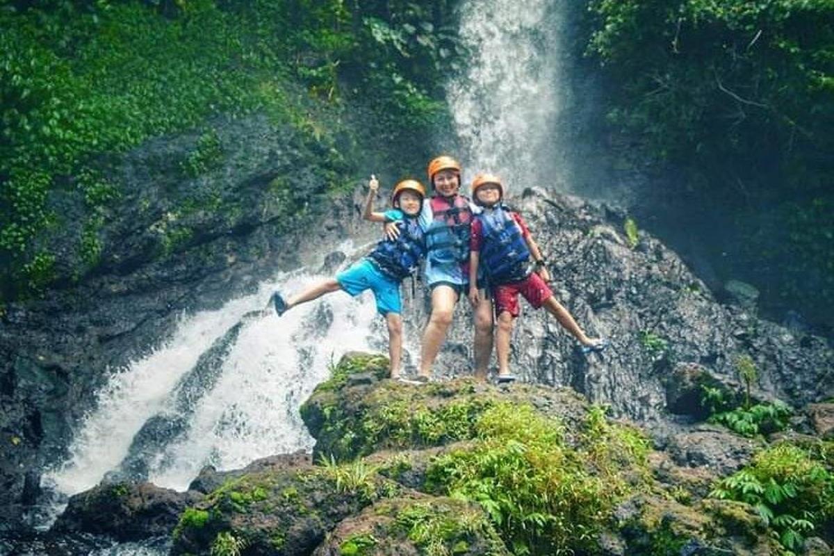 tiga orang berdiri di atas batu di hadapan air terjun