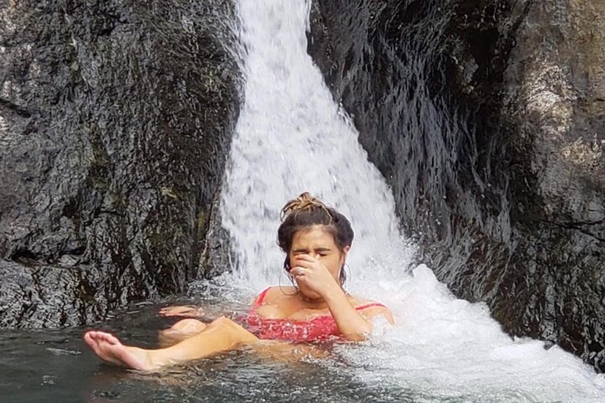 a girl sitting in the water in front of a waterfall