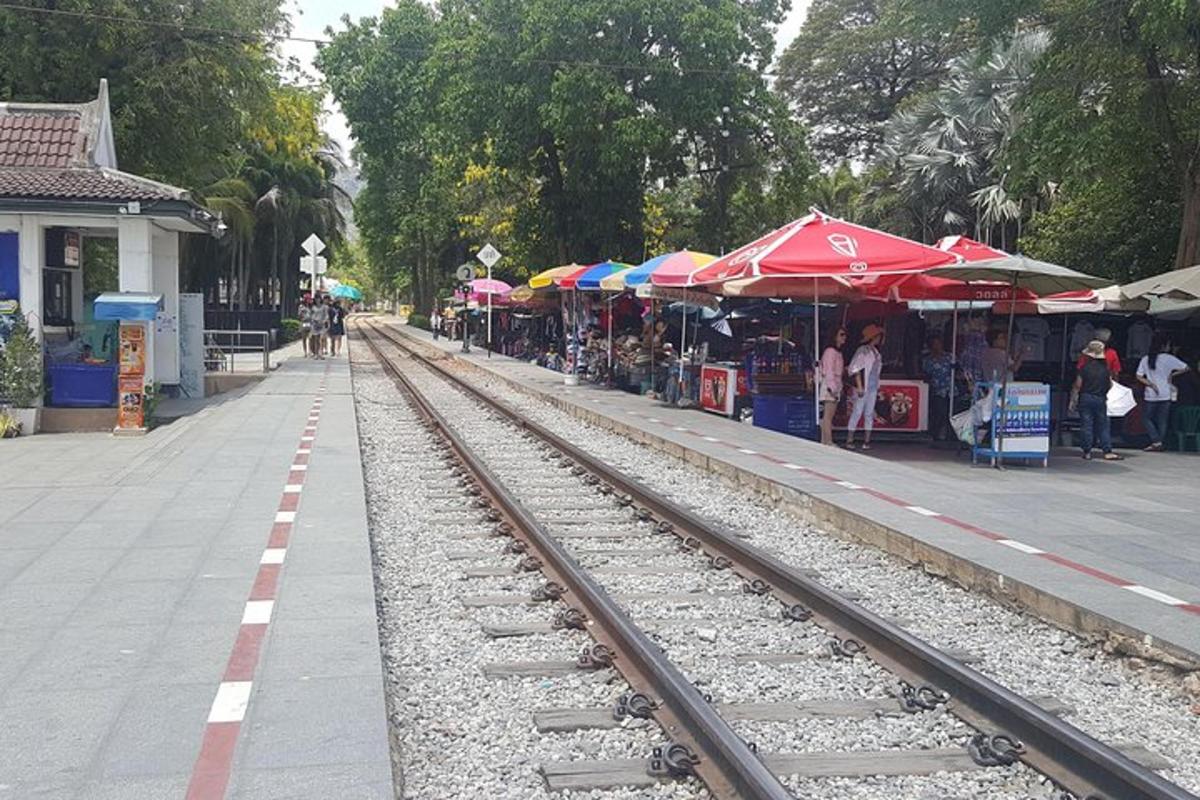 a train track next to an outdoor market with umbrellas