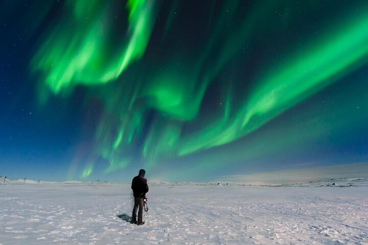 Maður stendur í snjónum undir norðurljósum