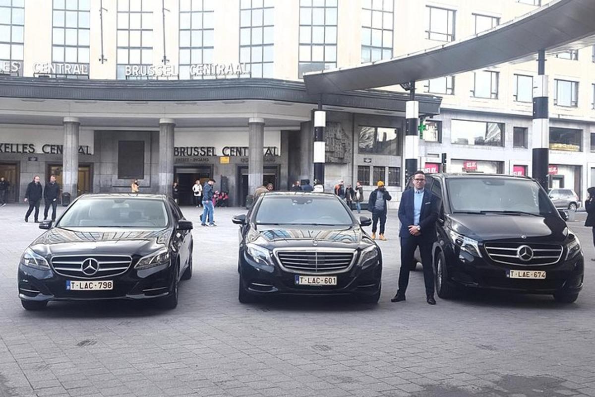 muž stojící mezi dvěma luxusními vozy před budovou