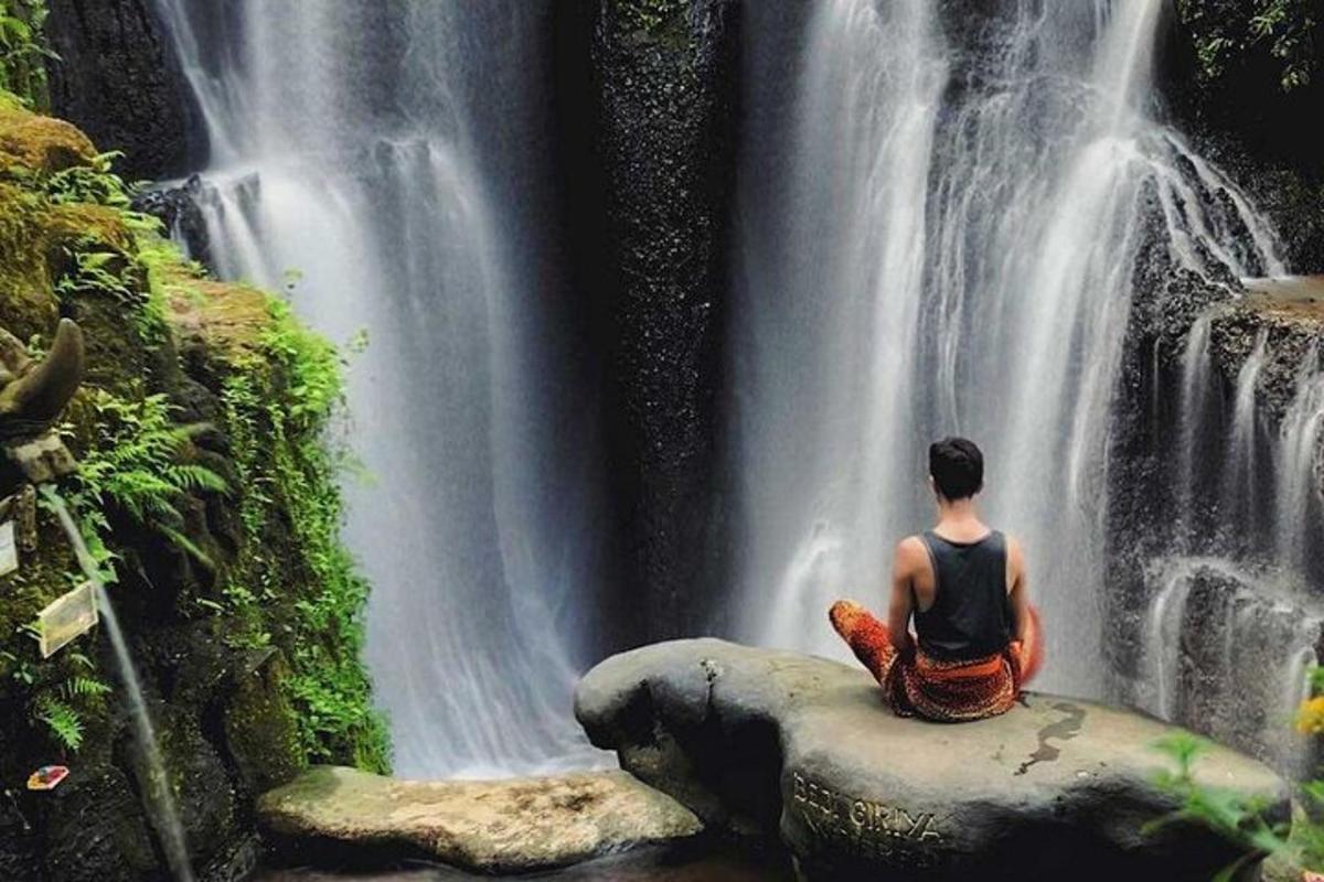 uma pessoa sentada em uma rocha em frente a uma cachoeira