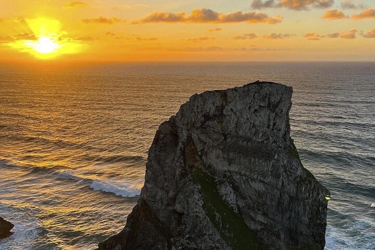 um pôr do sol sobre o oceano com uma grande rocha