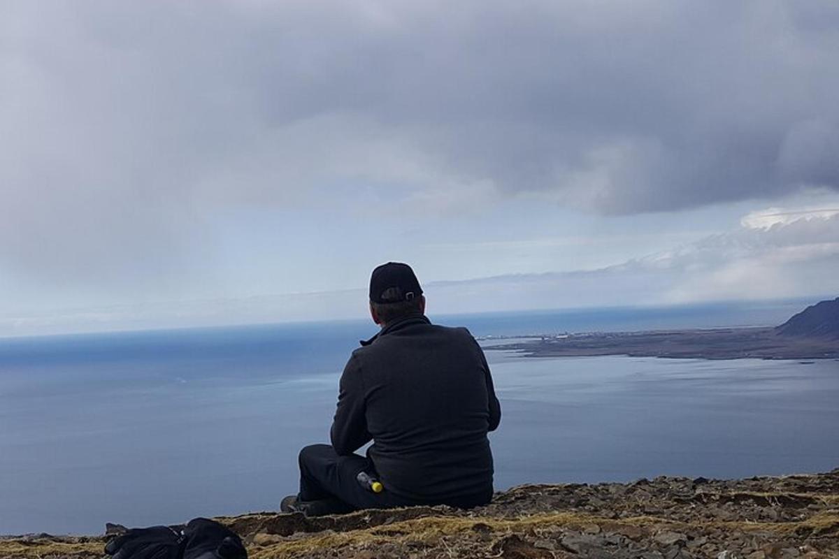 un home assegut en un turó mirant l'aigua