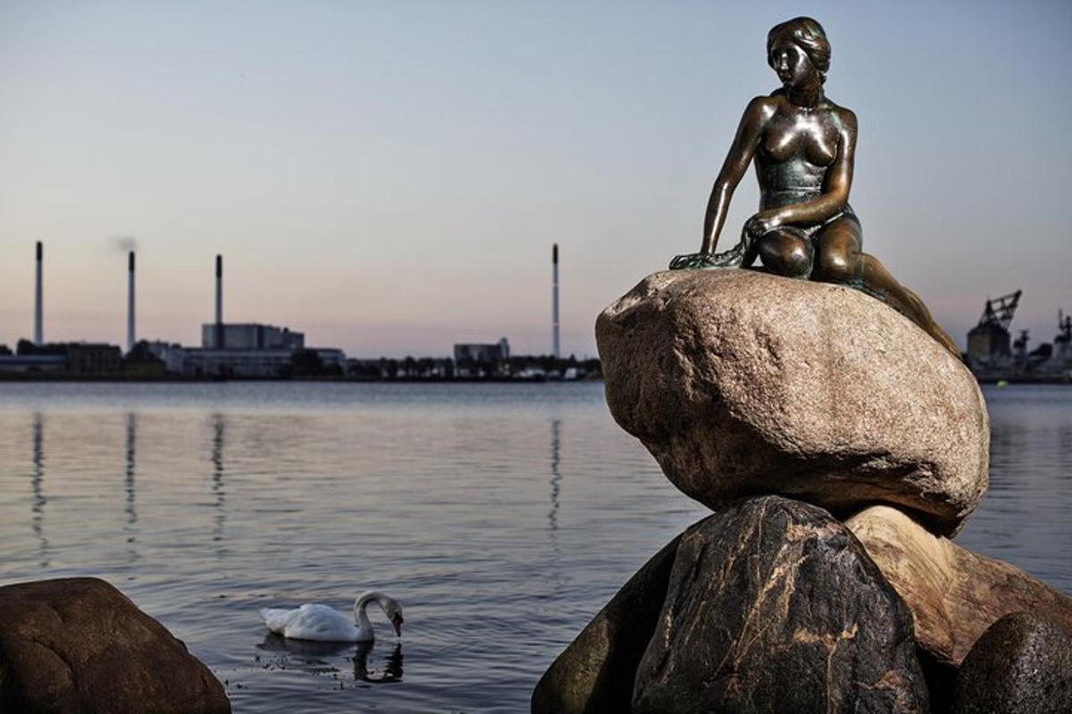 Una estatua de una niña sentada en una roca en el agua.
