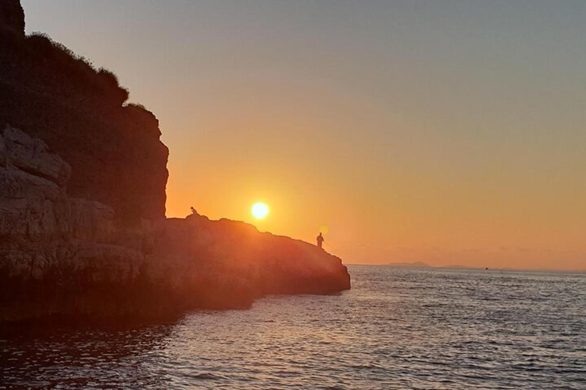 zachód słońca nad oceanem z osobą stojącą na klifie