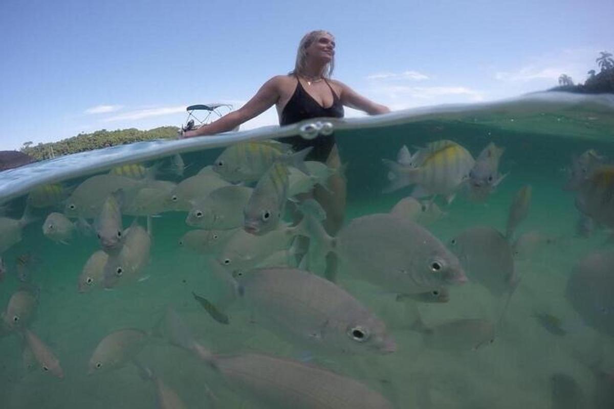 una dona que sosté una taula de surf a l'aigua amb un ramat de peixos