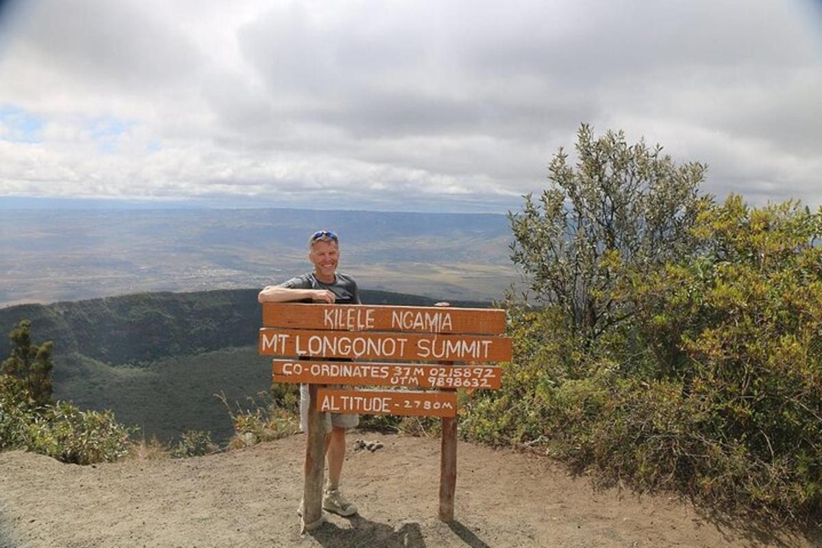un homme debout à côté d'un panneau sur une montagne