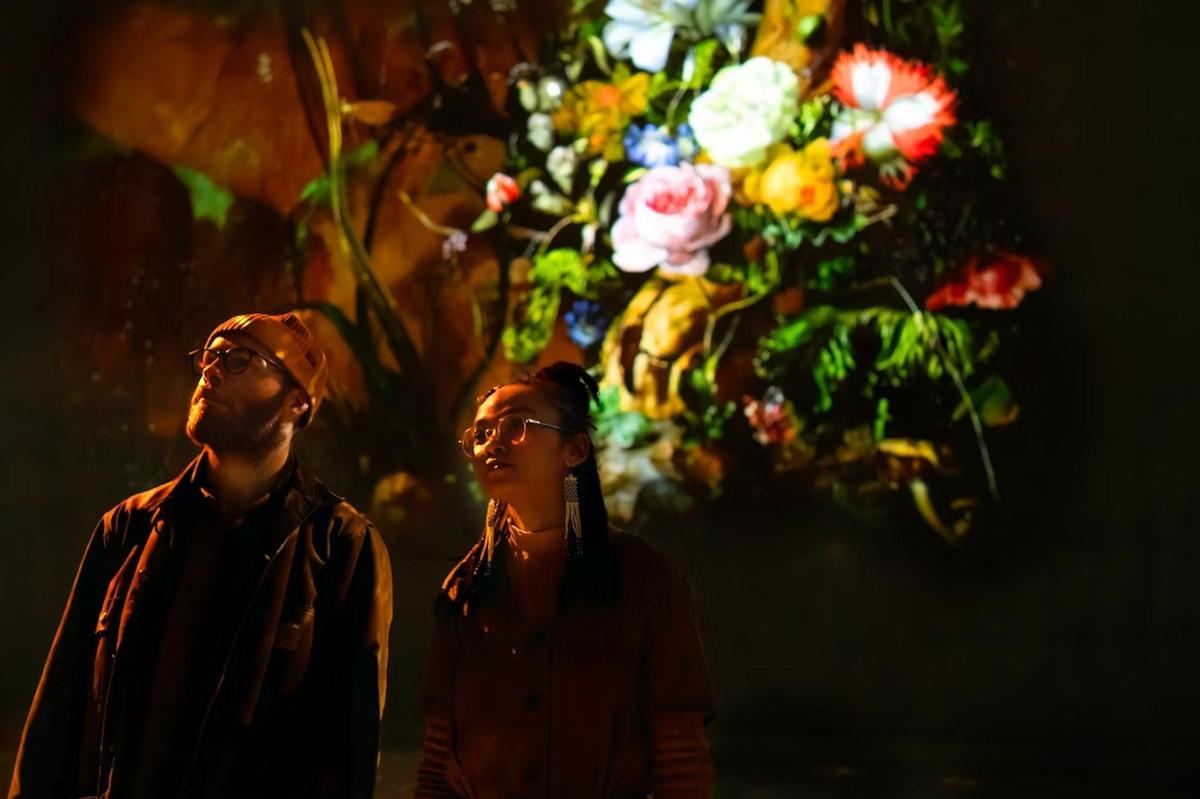 Un hombre y una mujer de pie frente a un arreglo floral.
