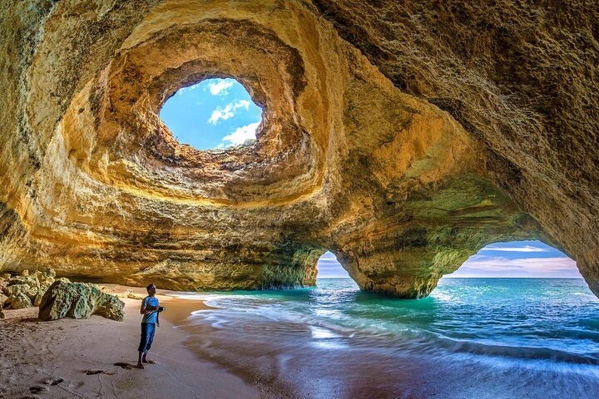 um homem parado na praia em frente a uma formação rochosa