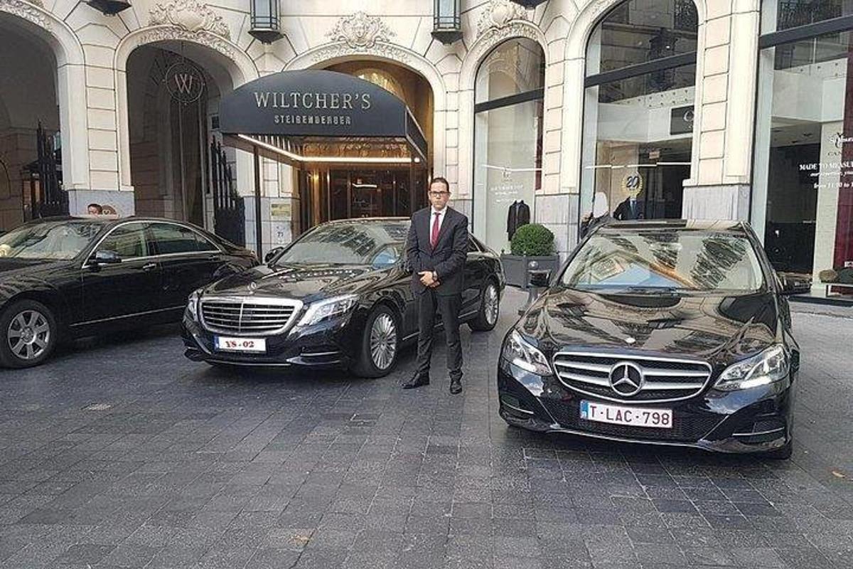 ein Mann im Anzug steht neben zwei Autos