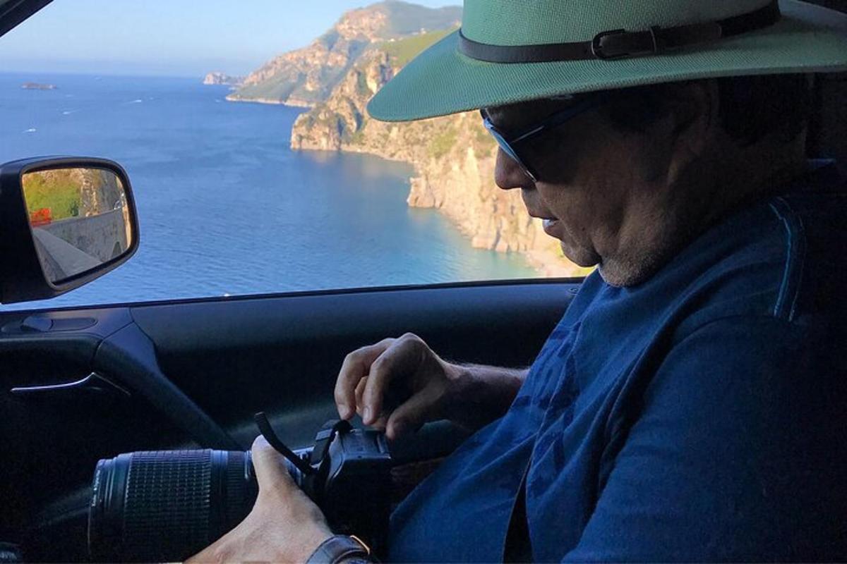 moški s klobukom sedi v avtu in gleda v svoj mobilni telefon