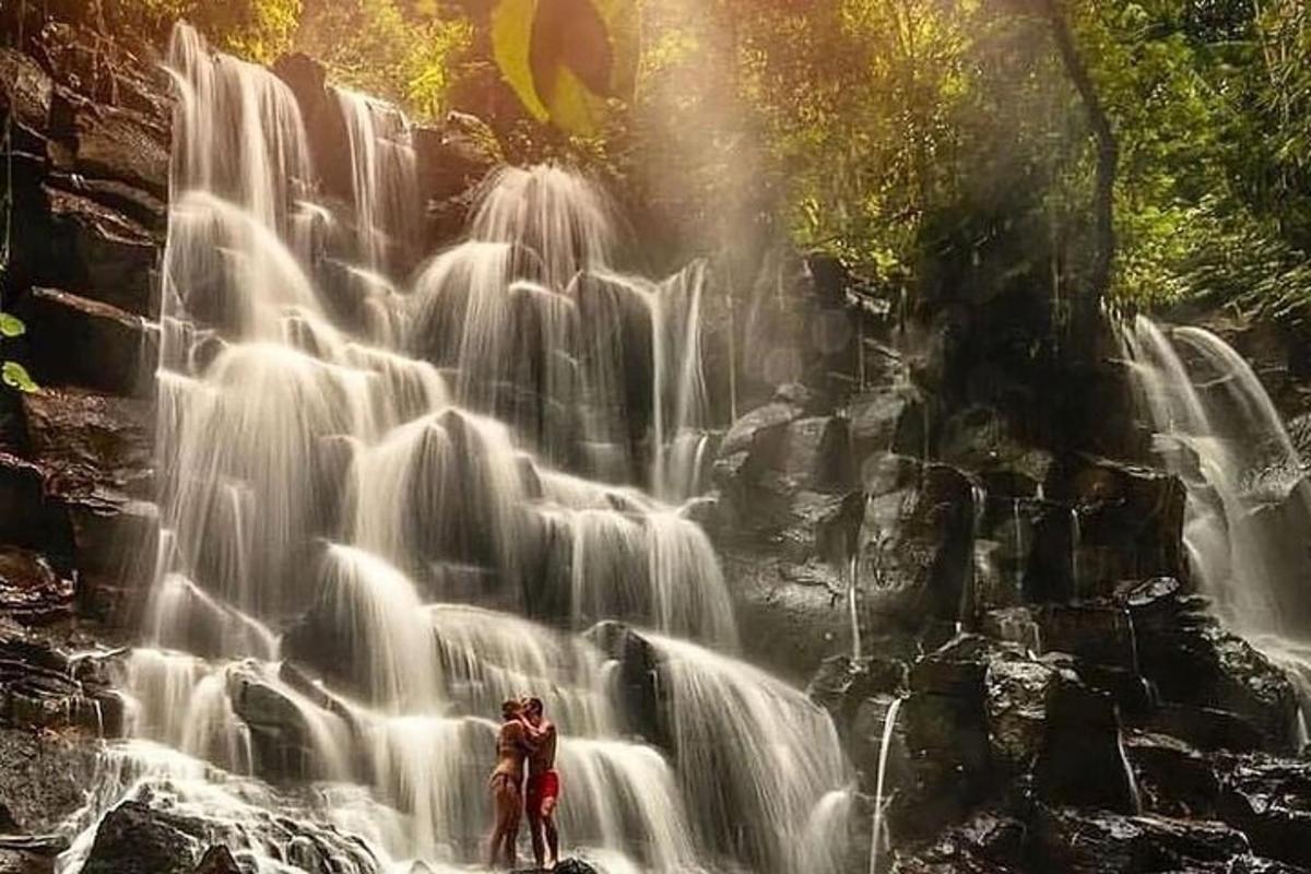 dua orang berdiri di hadapan air terjun