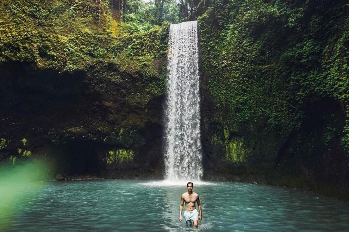 seorang lelaki berdiri di dalam air di hadapan air terjun