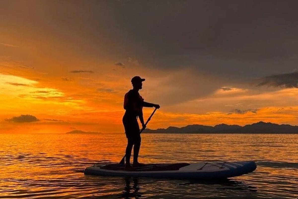 muž stojící na paddleboardu ve vodě při západu slunce