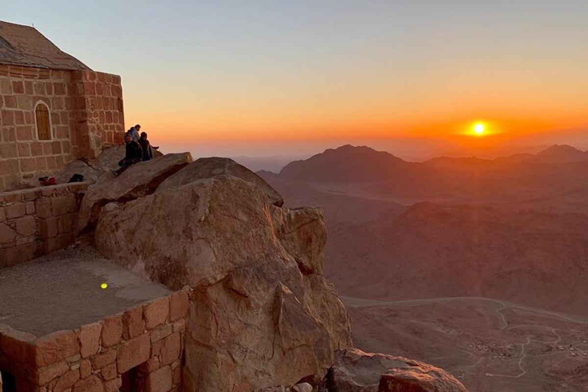 due persone sedute sul bordo di una montagna a guardare il tramonto
