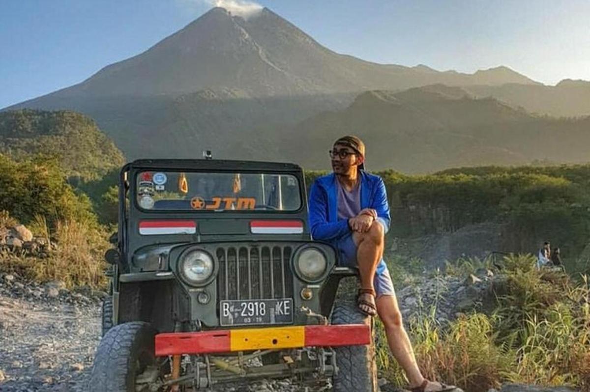 un uomo seduto sul davanti di una jeep con una montagna