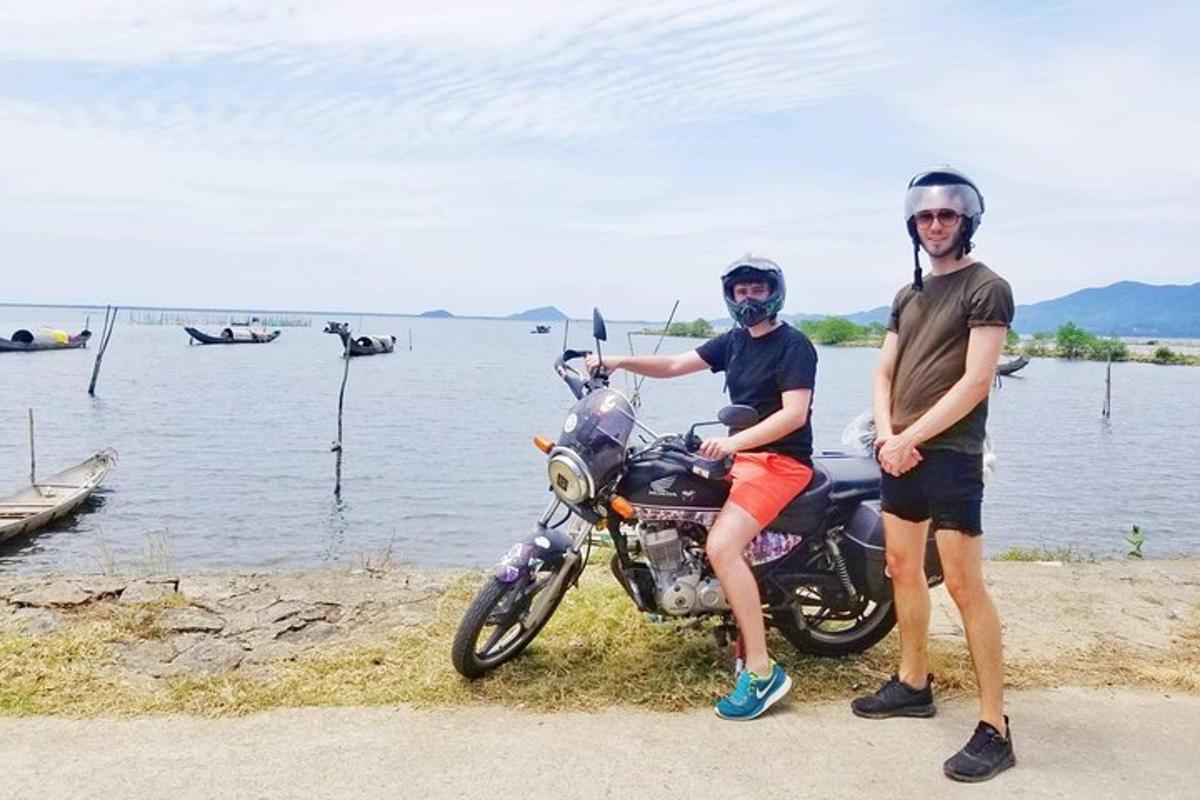 two men standing next to a motorcycle next to the water