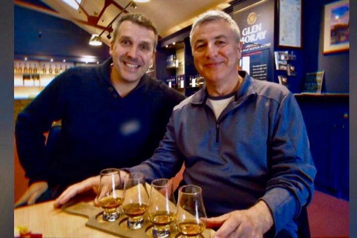 two men sitting at a bar with glasses of wine