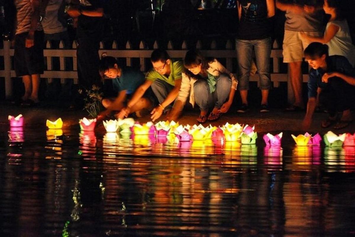 Un grupo de personas sentadas junto al agua con barquitos de papel.