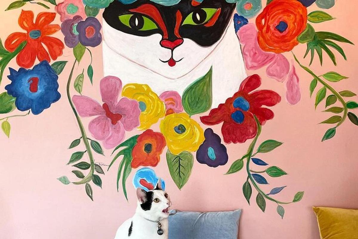 un gatto seduto su un cuscino davanti a un muro con un dipinto