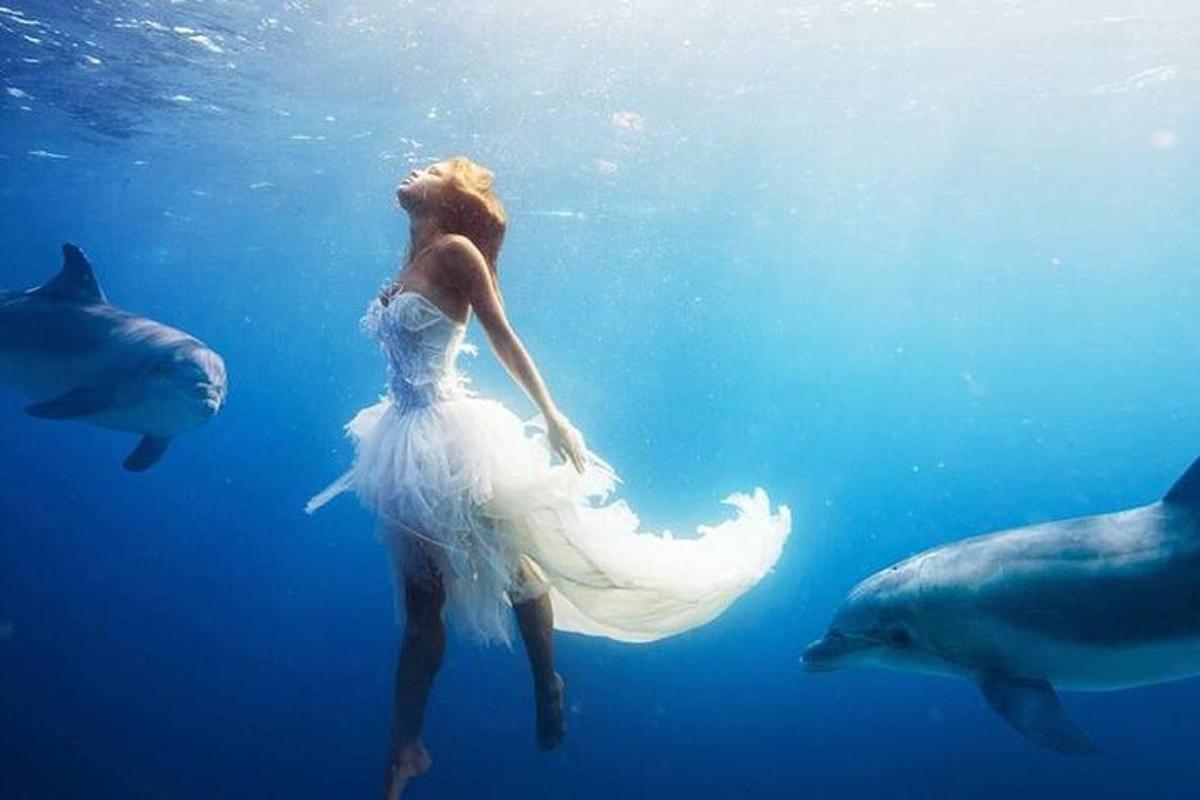 a woman in a wedding dress swimming in the water with dolphins