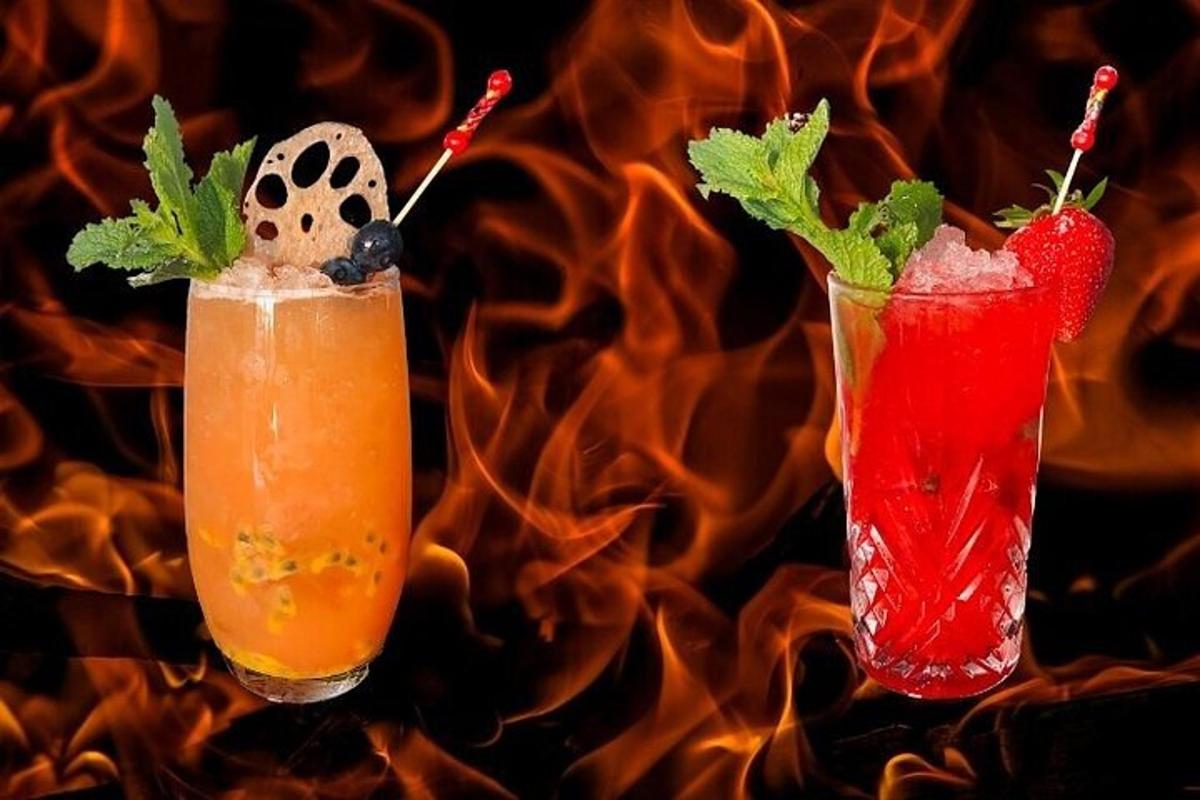 zwei Cocktails auf einem Tisch mit Feuer im Hintergrund