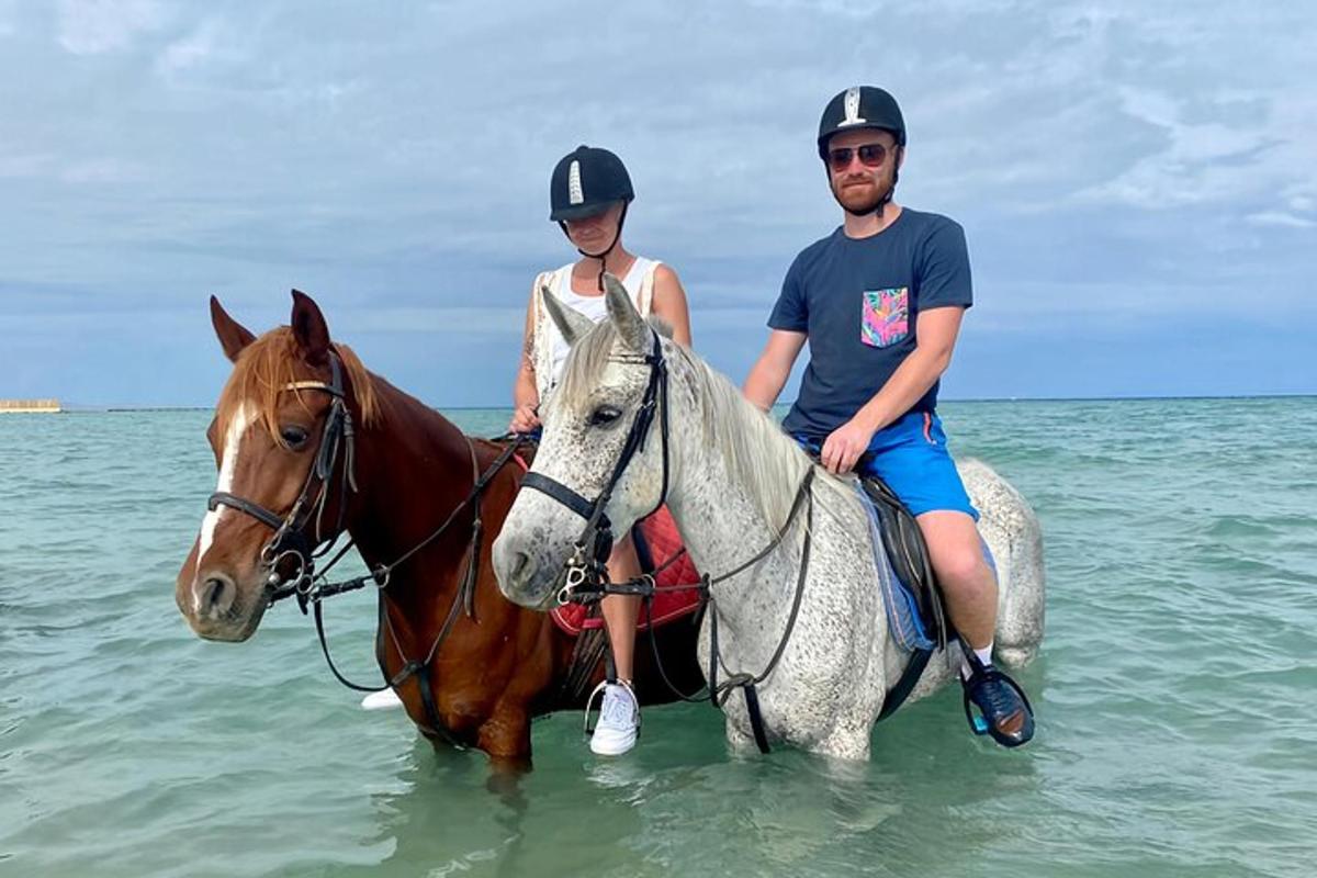 en mann og en kvinne som rir på en hest i havet