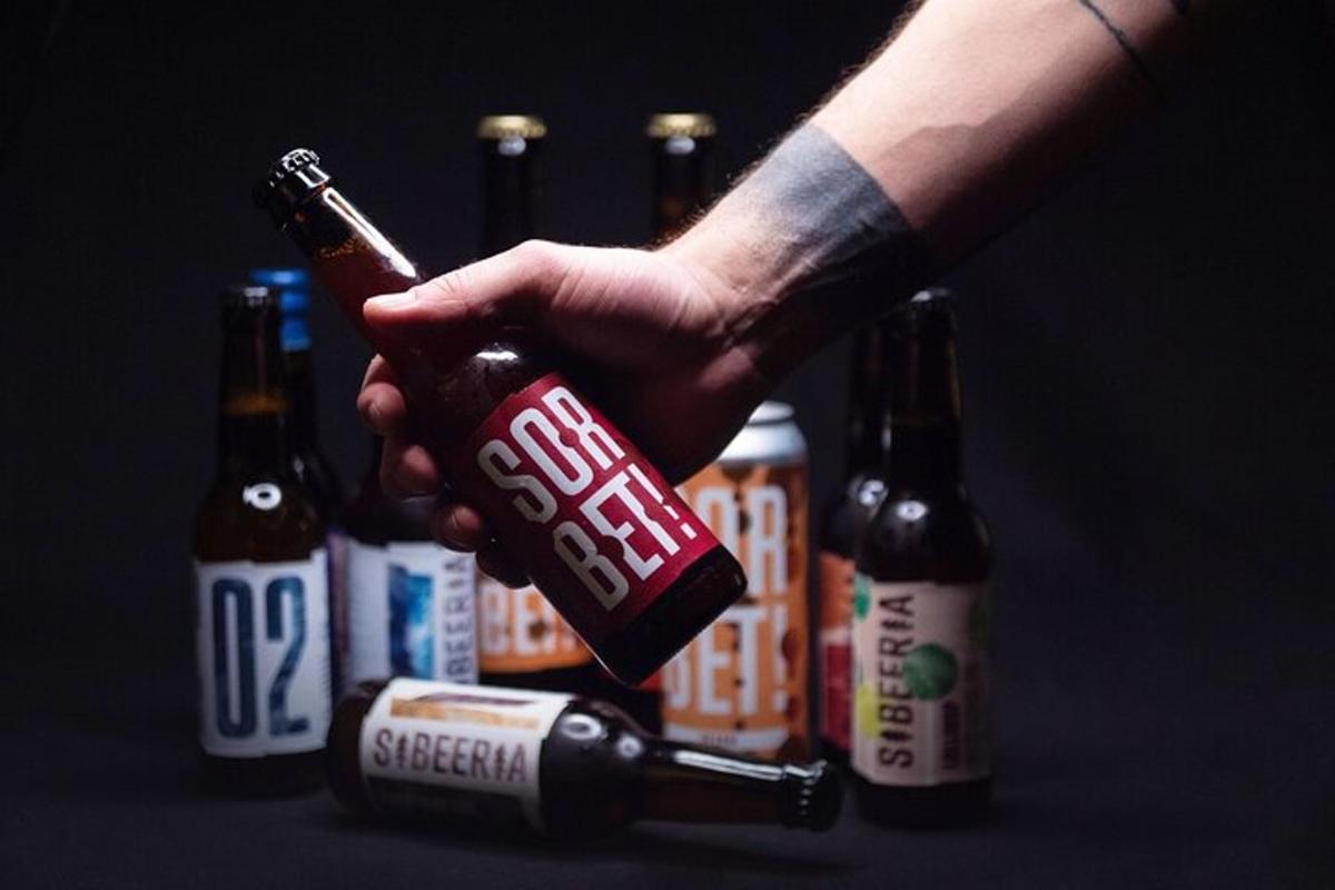 una persona che tiene una bottiglia di birra davanti a lattine di birra