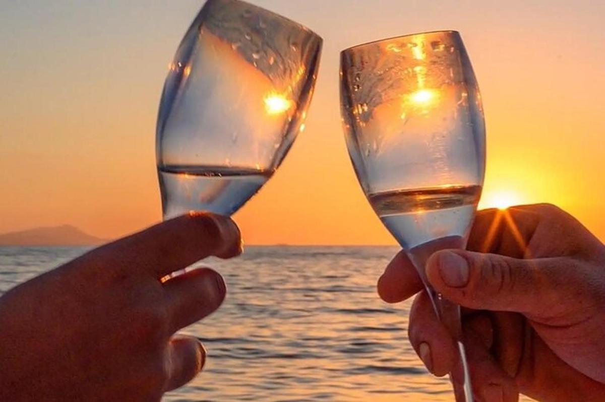 due persone che tengono in mano dei bicchieri di vino di fronte all'oceano