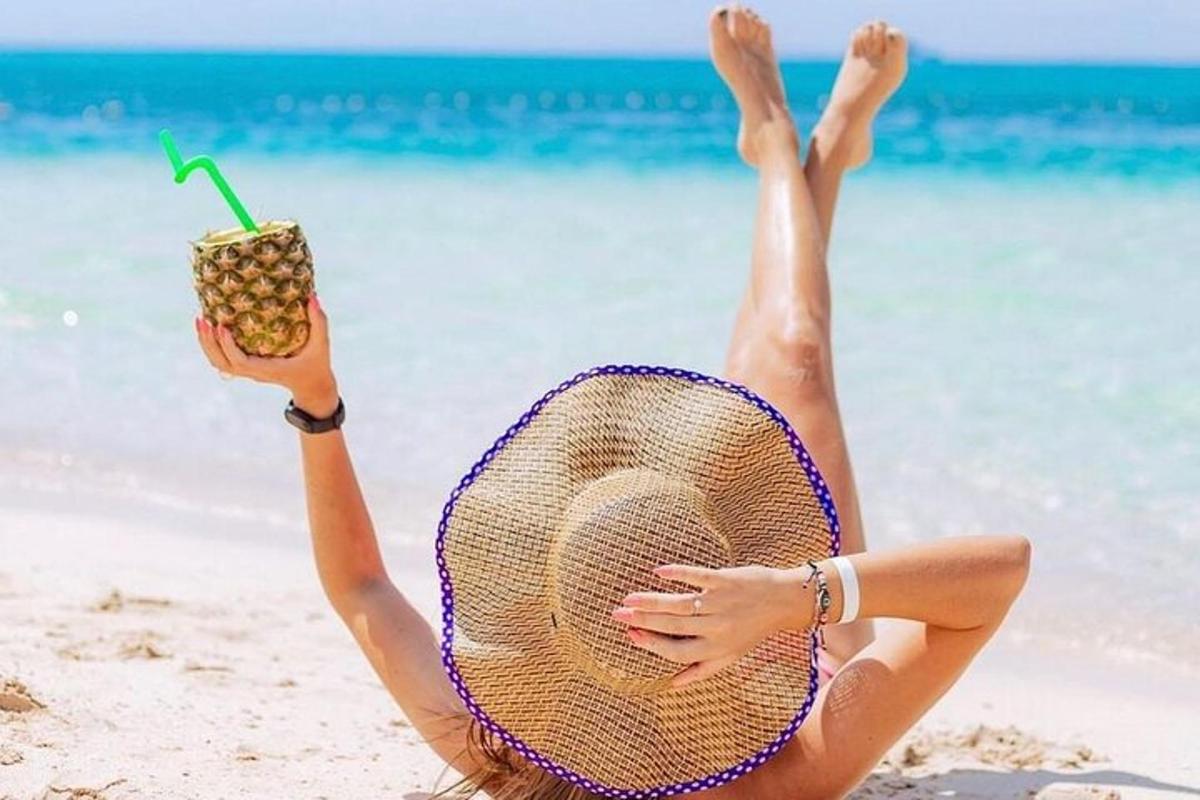 en kvinne som ligger på stranden med en stråhatt og en drink