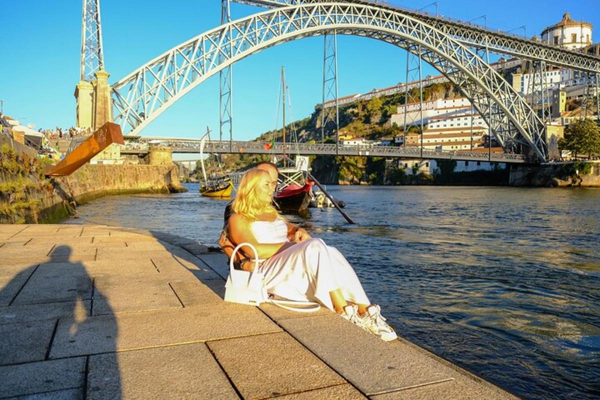 Una mujer sentada en la orilla de un río con un puente.