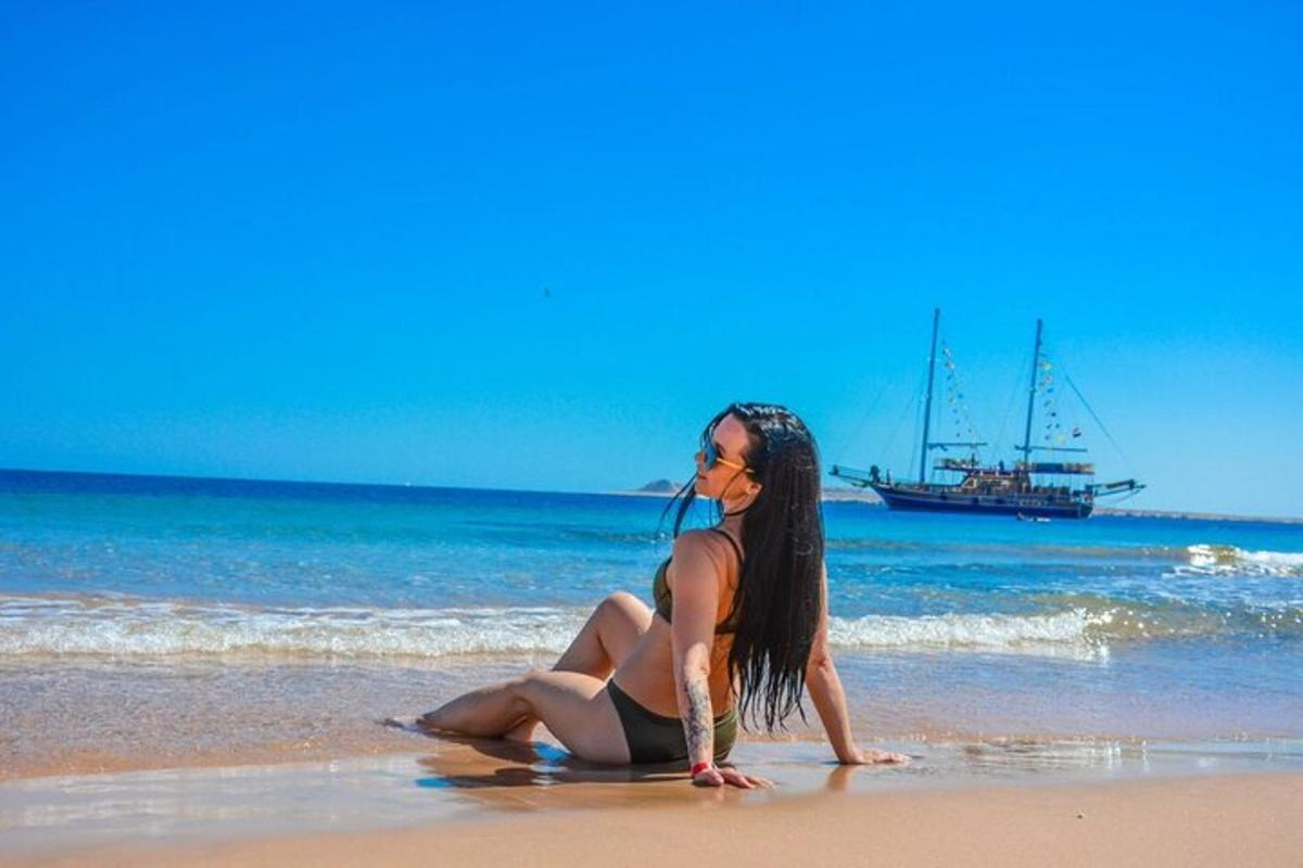 una donna seduta sulla spiaggia con una barca in acqua