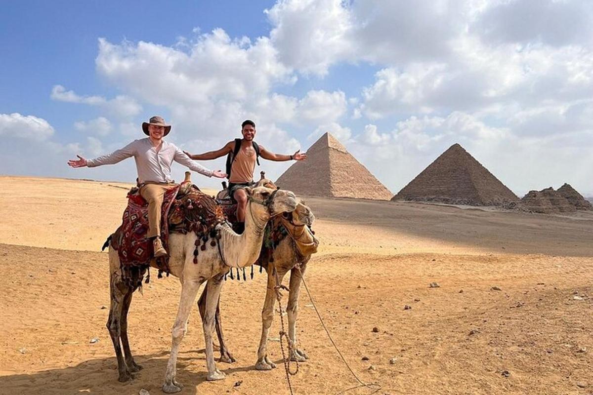 dva muži jedoucí na velbloudech před pyramidami